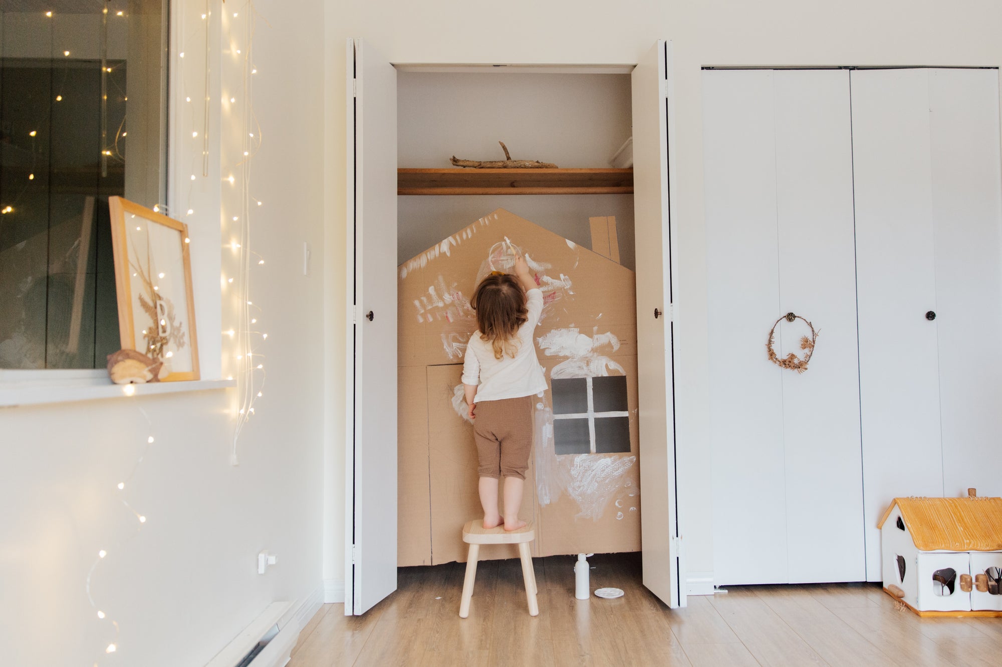 Toddler uses a stool to play with her doll house
